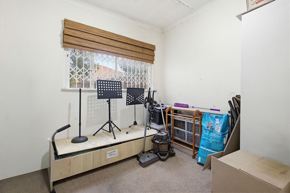 A small bedroom featuring carpet flooring, a window with a security gate, and a blind. The room requires cosmetic updates to the ceiling and walls.