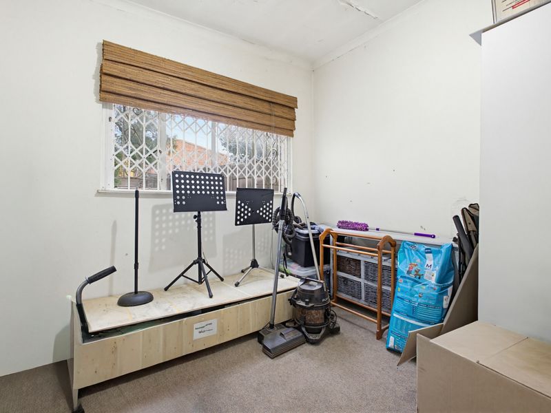 A small bedroom featuring carpet flooring, a window with a security gate, and a blind. The room requires cosmetic updates to the ceiling and walls.