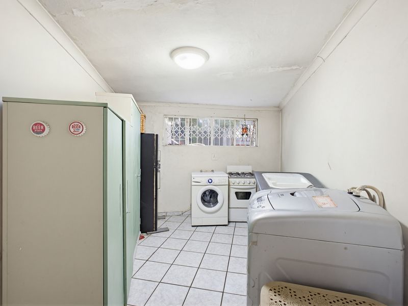 A functional laundry room featuring tiled flooring, security window bars, and built-in cabinetry, requiring some cosmetic updates to the ceiling and wall finishes.