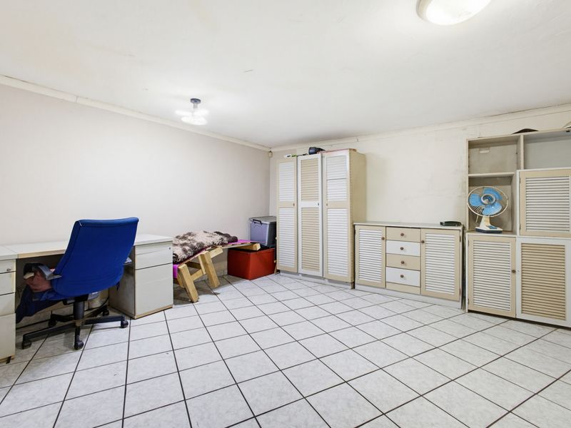 A functional office space featuring tiled flooring and extensive built-in cabinetry, currently used as a multi-purpose storage and workspace area.