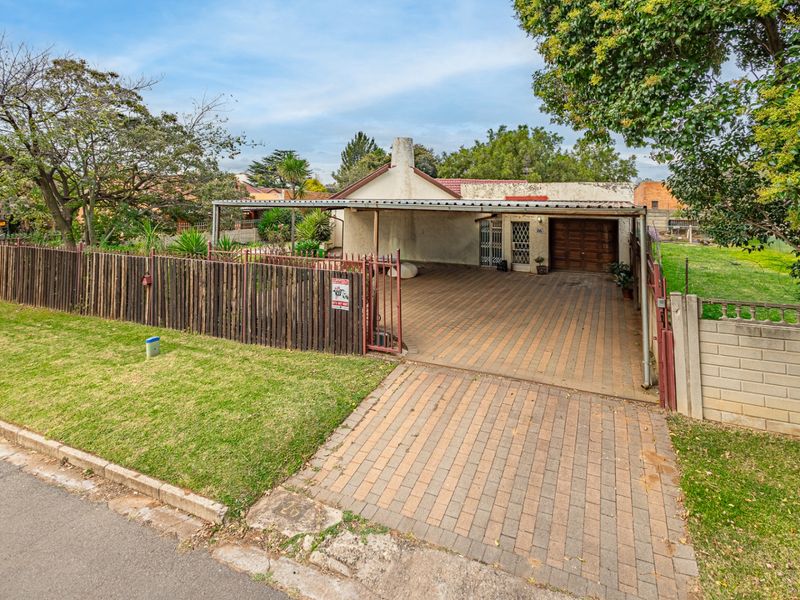 Front view of a residential property featuring a paved driveway, covered carport, secure garage access, and established garden boundaries.