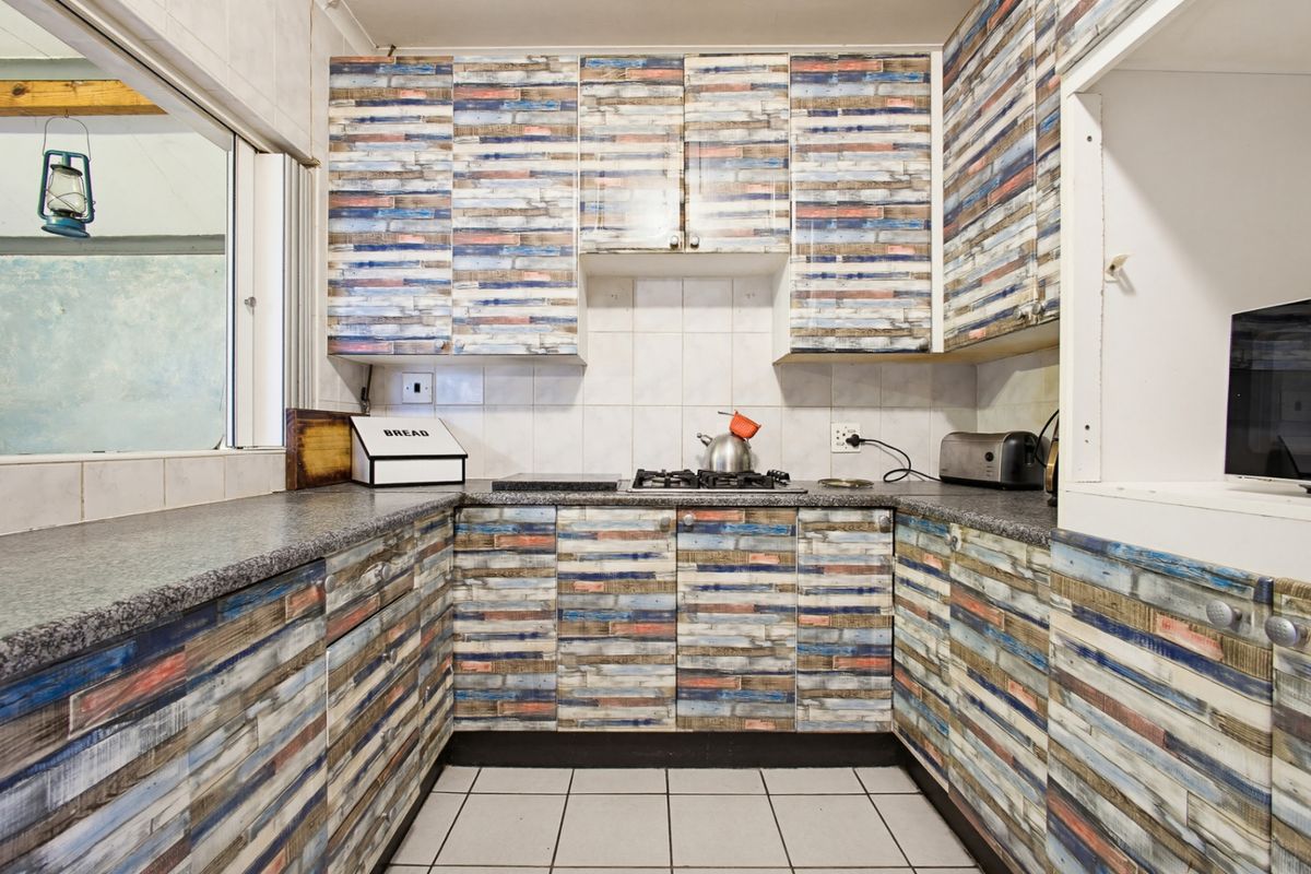 Compact kitchen featuring U-shaped layout with gas hob, tiled splashbacks, and patterned cabinetry finish.