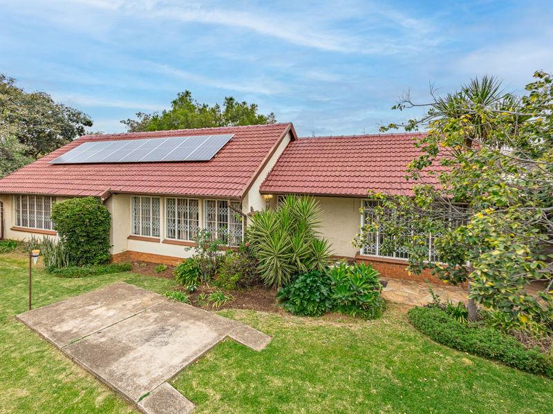 Rear view of the house featuring a tiled roof with solar panels, security-barred windows, and a well-maintained garden with a concrete patio area.