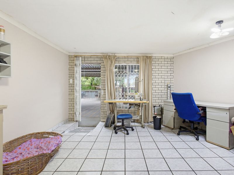 A functional office space featuring tiled flooring, a brick feature wall, and direct access to an outdoor patio area through a security gate.