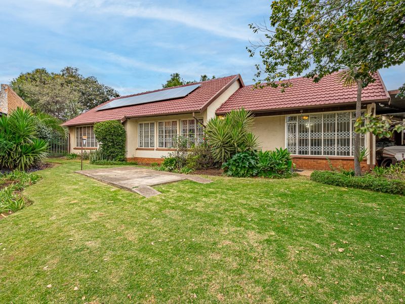 Rear view of the house featuring a tiled roof with solar panels, security-barred windows, and a spacious garden with a concrete patio area.