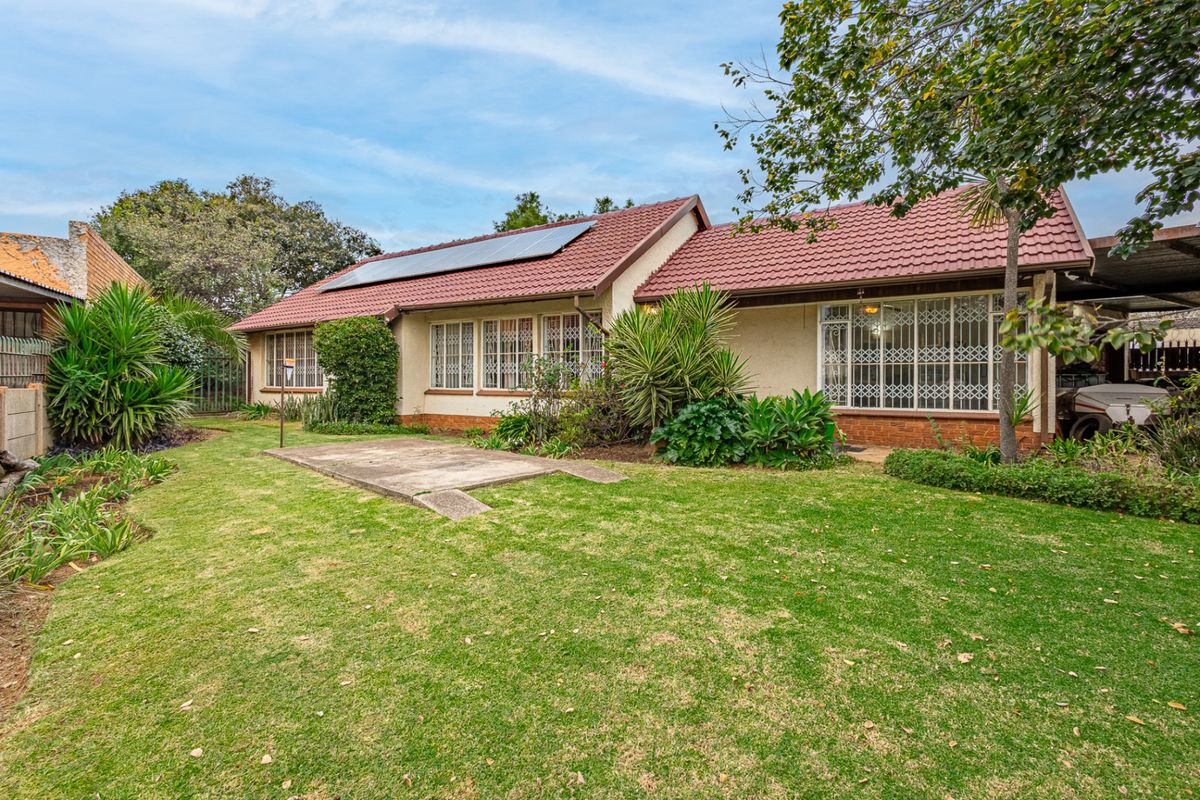 Rear view of the house featuring a tiled roof with solar panels, security-barred windows, and a spacious garden with a concrete patio area.