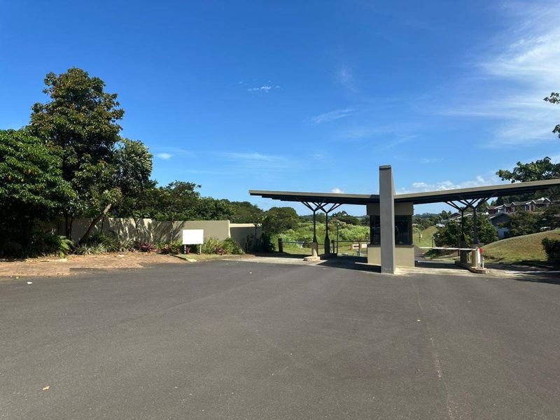 A view of the residential estate entrance featuring a modern security gatehouse, boom gate, and paved driveway access.