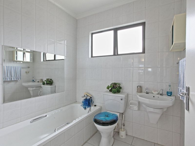 A functional bathroom featuring a bathtub, wall-mounted basin, and toilet, finished with white wall and floor tiles and a large mirror.