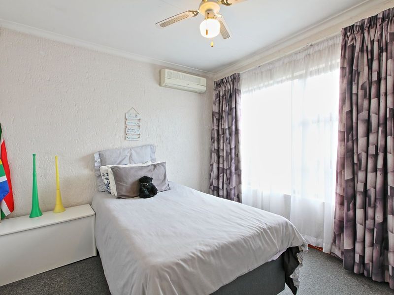 A functional bedroom featuring a ceiling fan, wall-mounted air conditioning unit, and carpeted flooring, providing a comfortable living space.