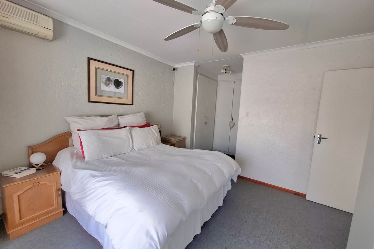 A bedroom featuring a ceiling fan, wall-mounted air conditioning unit, and built-in cupboards with carpeted flooring.