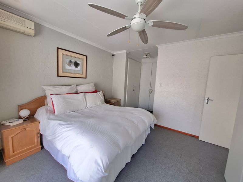 A bedroom featuring a ceiling fan, wall-mounted air conditioning unit, and built-in cupboards with carpeted flooring.