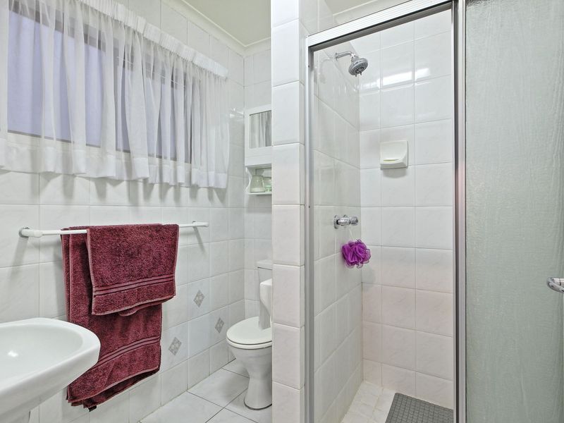 A functional bathroom featuring a shower enclosure, pedestal basin, and toilet with neutral wall and floor tiling.