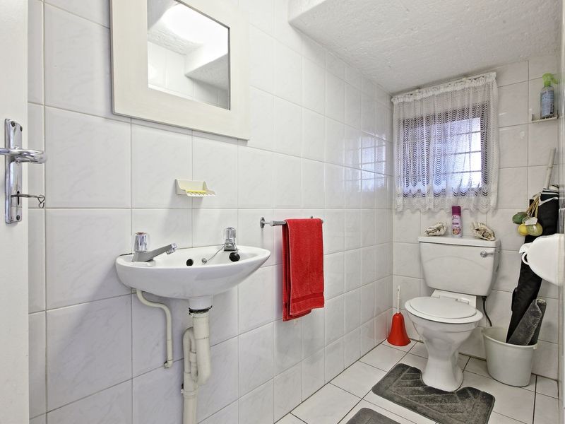 A functional bathroom featuring white wall tiles, a wall-mounted basin, and a standard toilet, offering a clean and practical layout.