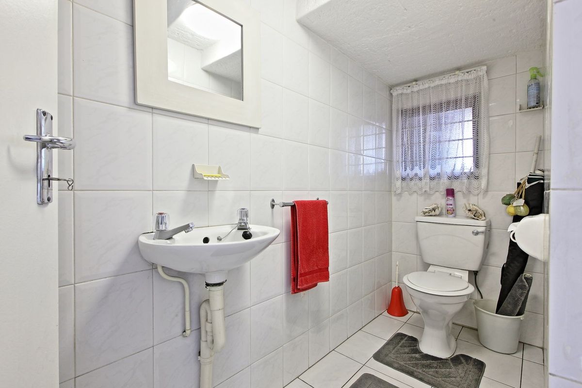 A functional bathroom featuring white wall tiles, a wall-mounted basin, and a standard toilet, offering a clean and practical layout.