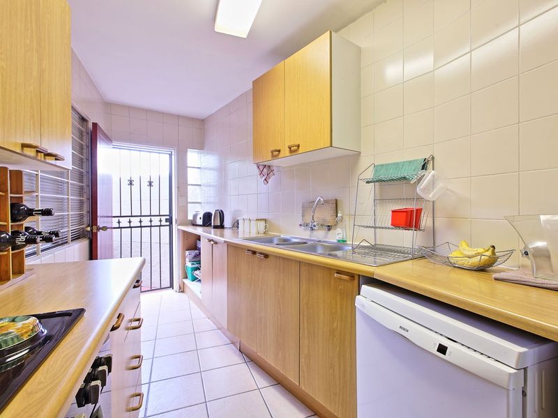 A functional galley-style kitchen featuring wood-finish cabinetry, laminate countertops, tiled walls, and direct access to an exterior security gate.
