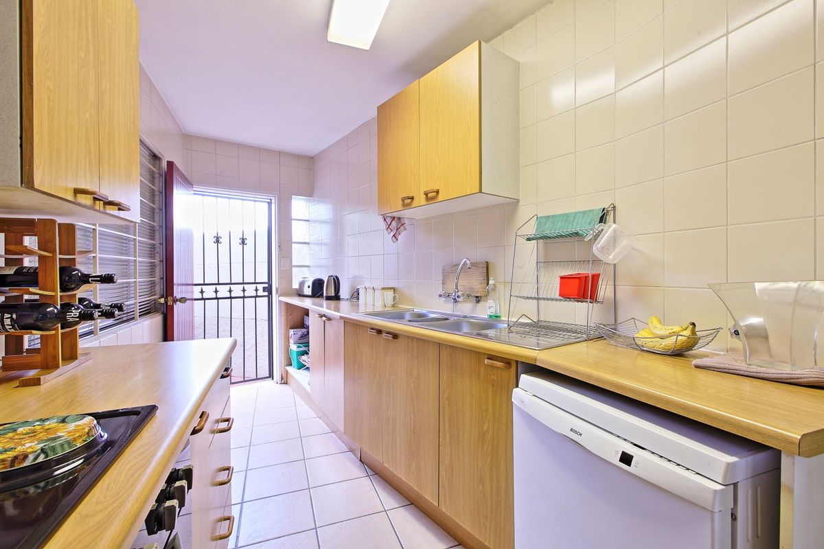 A functional galley-style kitchen featuring wood-finish cabinetry, laminate countertops, tiled walls, and direct access to an exterior security gate.