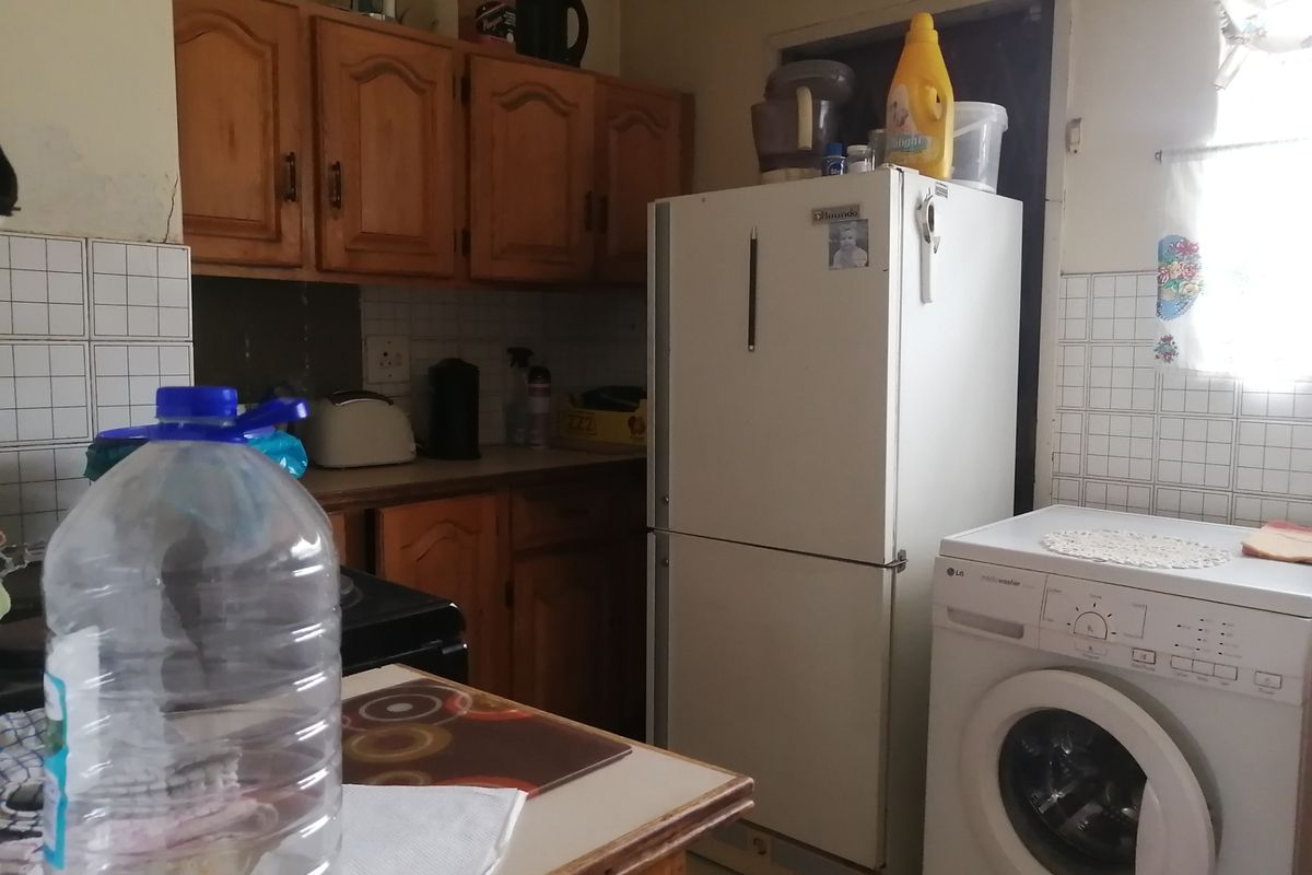 A dated kitchen featuring wooden cabinetry, tiled splashbacks, and integrated space for laundry appliances.