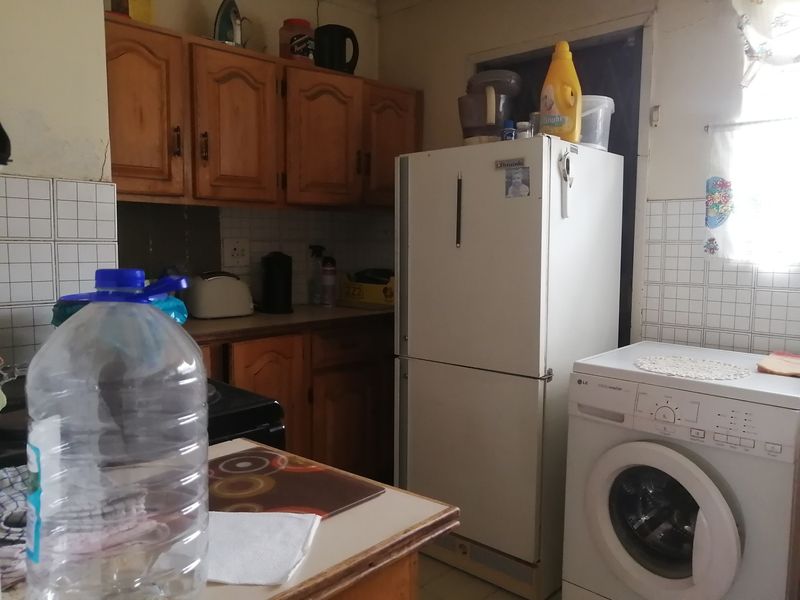 A dated kitchen featuring wooden cabinetry, tiled splashbacks, and integrated space for laundry appliances.