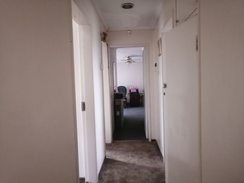A narrow residential hallway connecting multiple rooms, featuring neutral wall finishes and carpeted flooring.