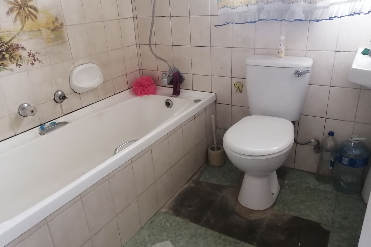 A dated bathroom featuring a standard bathtub, toilet, and tiled finishes, currently requiring cosmetic updates and floor repairs.