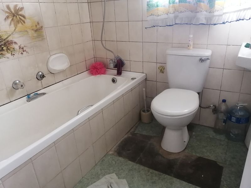 A dated bathroom featuring a standard bathtub, toilet, and tiled finishes, currently requiring cosmetic updates and floor repairs.