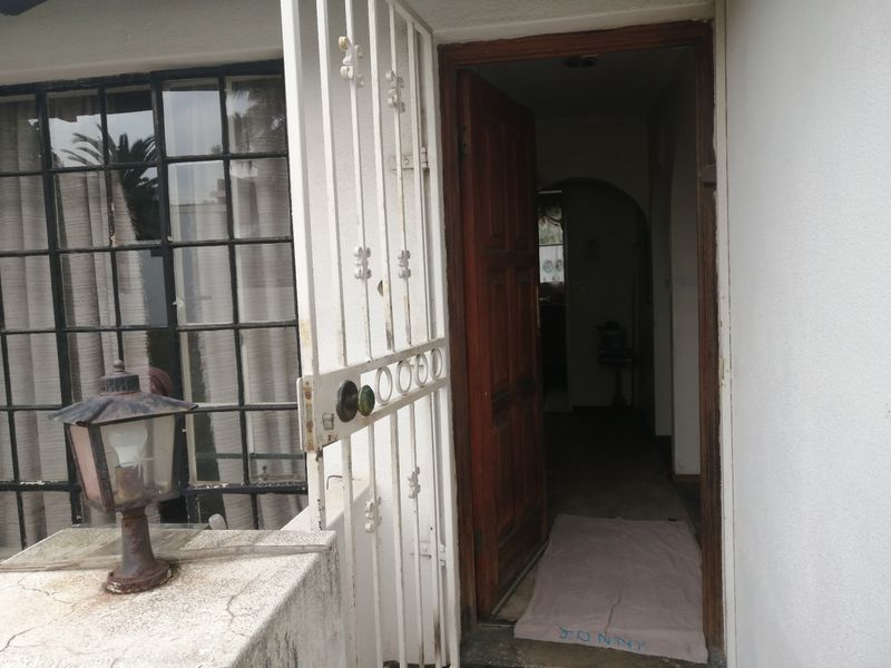 Front entrance featuring a security gate, timber door, and exterior lighting, showing signs of wear and requiring maintenance.
