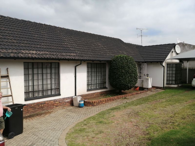 Front elevation of a single-story house featuring a tiled roof, brick base, and security-barred windows with a paved walkway leading to the entrance.