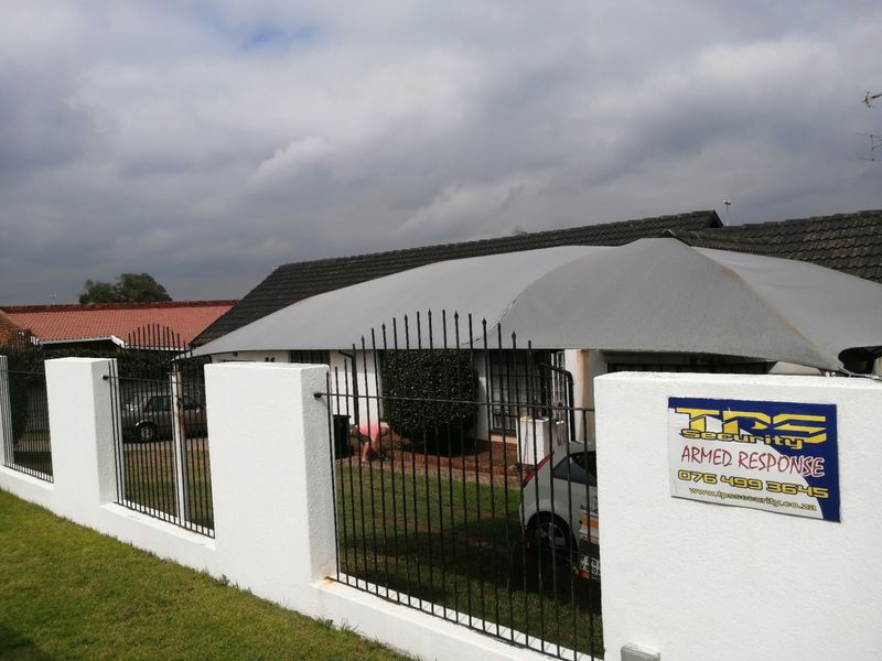 Front view of the property featuring a perimeter wall with metal security fencing and a large shade sail covering the driveway area.