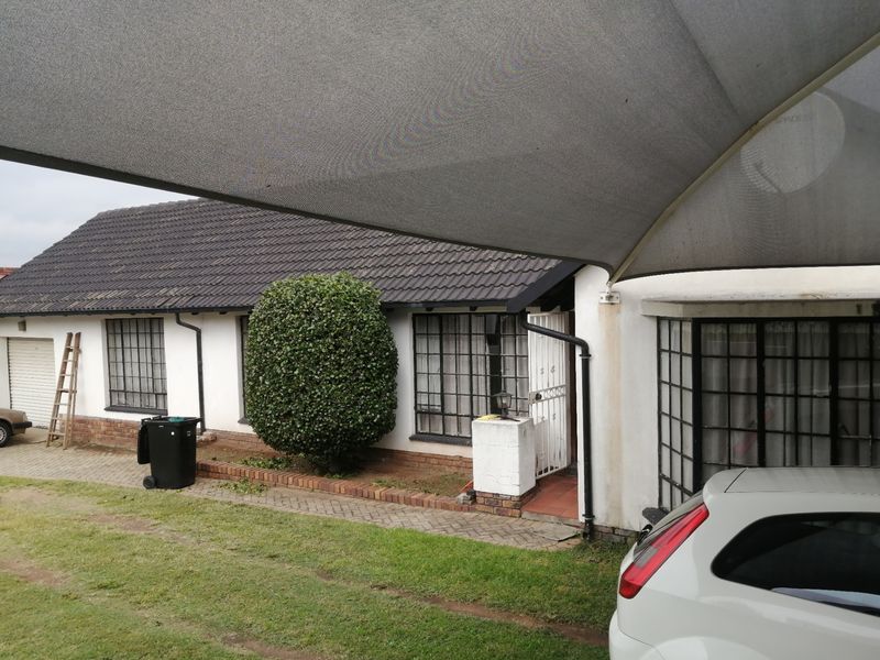 Front elevation of a single-story house featuring a tiled roof, security bars on windows, and a paved driveway area with a shade sail.