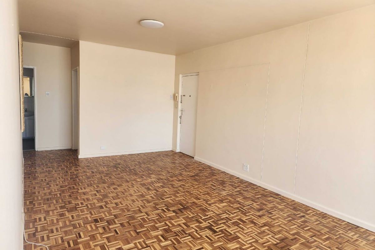 An empty living room featuring traditional parquet flooring, neutral wall tones, and an integrated intercom system, offering a blank canvas for renovation.