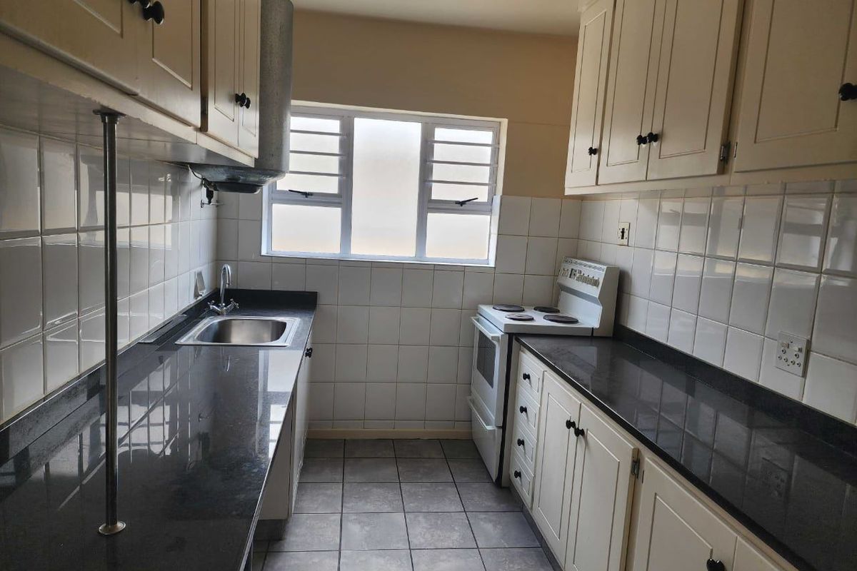 A functional galley-style kitchen featuring stone countertops, tiled backsplash, ample cabinetry, and a freestanding stove with a window for natural light.