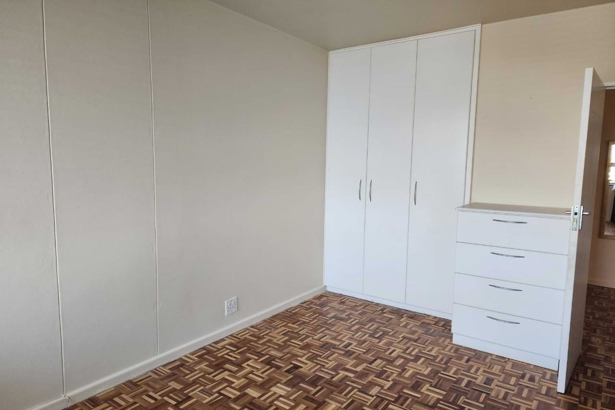 A clean, empty bedroom featuring classic parquet flooring and a white built-in wardrobe, offering a neutral canvas for personalization.