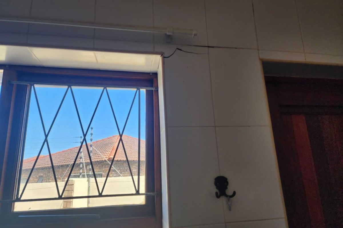 A close-up view of a tiled kitchen wall featuring a window with security bars and a visible crack in the tiling.