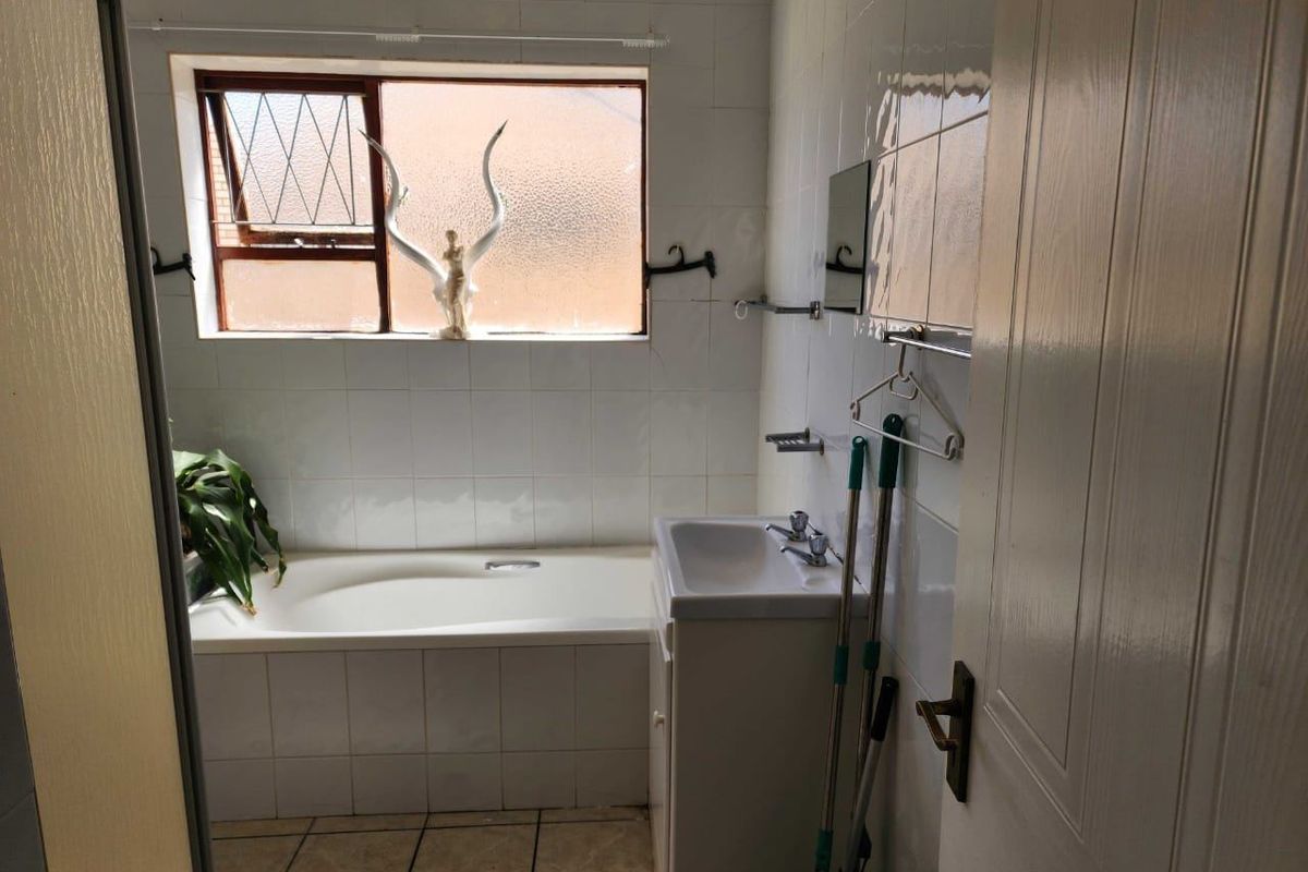 A dated bathroom featuring a built-in bathtub, vanity basin, and tiled finishes, requiring cosmetic updates to modernize the space.