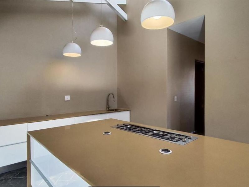 Modern kitchen featuring a large island with a built-in gas cooktop, stone countertops, sleek cabinetry, and contemporary pendant lighting.