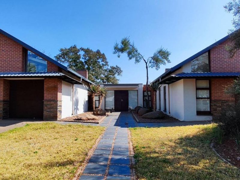 A well-maintained modern house featuring a brick and plaster facade, double garage, and a paved central walkway leading to the main entrance.