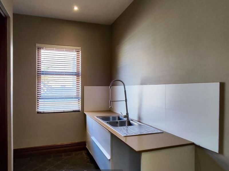 A functional scullery area featuring a stainless steel sink, gooseneck mixer tap, tiled splashback, and built-in cabinetry with neutral wall finishes.