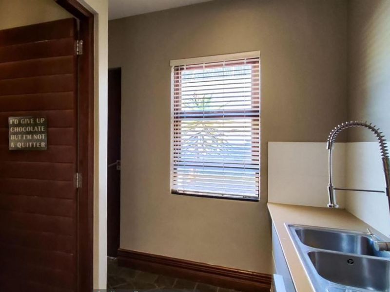 A functional scullery area featuring a double bowl sink with a modern gooseneck mixer tap, stone flooring, and a window with venetian blinds.