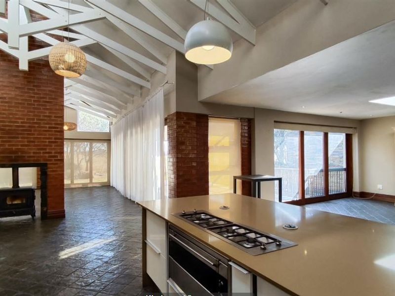 Spacious open-plan living area featuring exposed timber trusses, a brick fireplace with a wood-burning stove, slate flooring, and a modern kitchen island.
