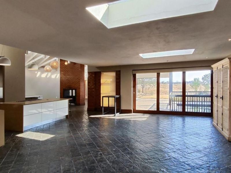 Spacious open-plan living area featuring stone tile flooring, large skylights, a modern kitchen island, and sliding glass doors leading to the exterior.
