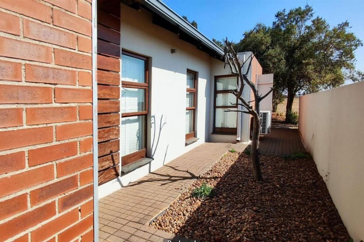 A well-maintained rear exterior area featuring a brick and timber facade, paved walkway, and a low-maintenance pebble garden.