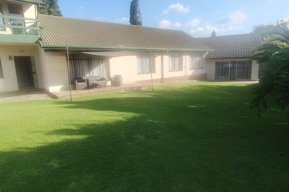 A spacious rear garden featuring a well-maintained lawn, a paved patio area, and a multi-level house structure with a balcony and tiled roof.
