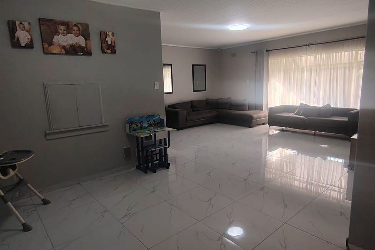 Spacious living room featuring polished marble-look floor tiles, a white tongue and groove timber ceiling, and ample natural light through large windows.