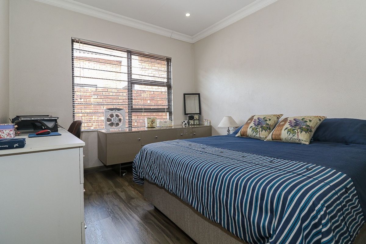 A well-maintained bedroom featuring wood-look flooring, recessed ceiling lighting, and a large window with fitted blinds.