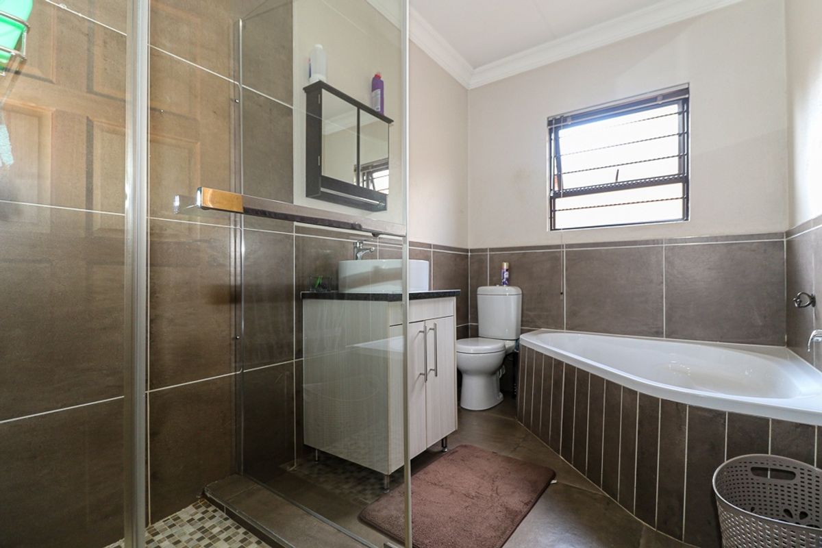A functional bathroom featuring a glass-enclosed shower, a corner bathtub, a vanity cabinet with a basin, and a window for natural light.