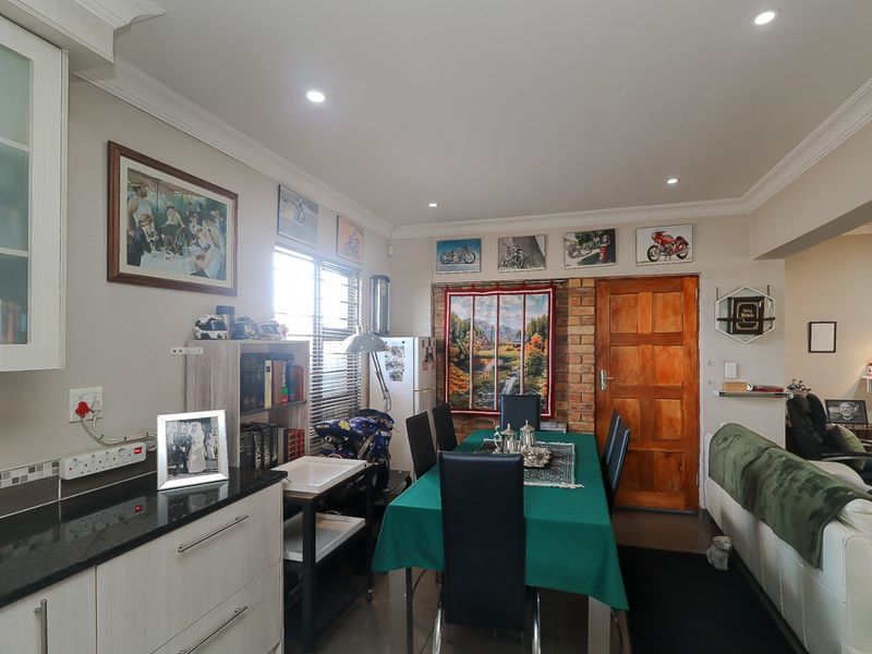 Open plan dining area featuring tiled flooring, recessed ceiling lighting, and a feature brick wall with a solid timber door.