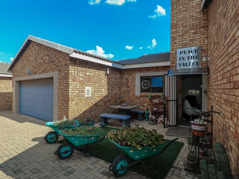 Exterior view of a face-brick cluster home featuring a paved driveway, single garage, and a small private entrance patio area.