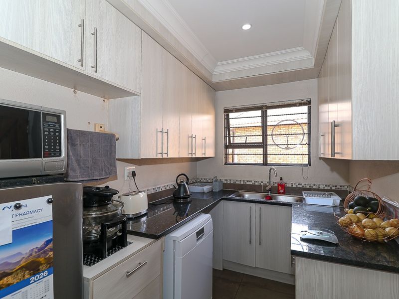 Compact kitchen featuring light wood-grain cabinetry, dark granite countertops, a stainless steel sink, and integrated space for a dishwasher.