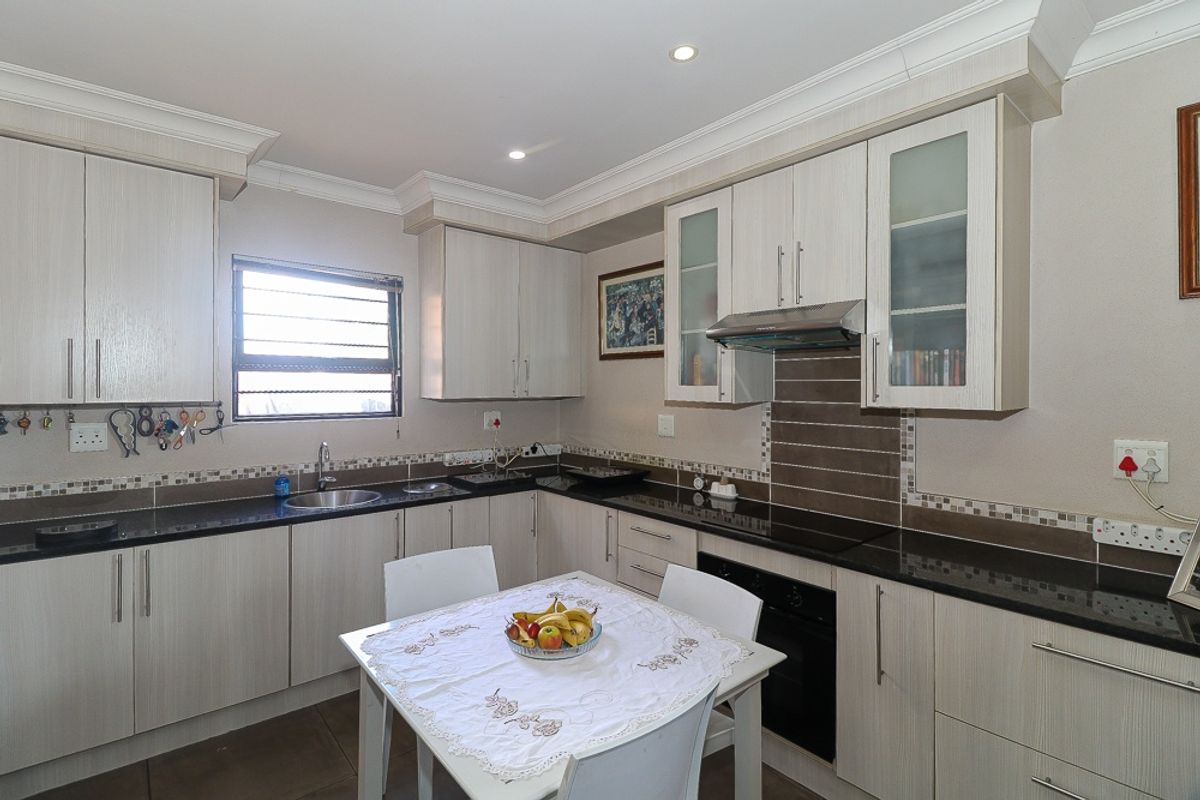 A well-maintained kitchen featuring light wood-grain cabinetry, dark granite countertops, a built-in oven, extractor fan, and a tiled backsplash.