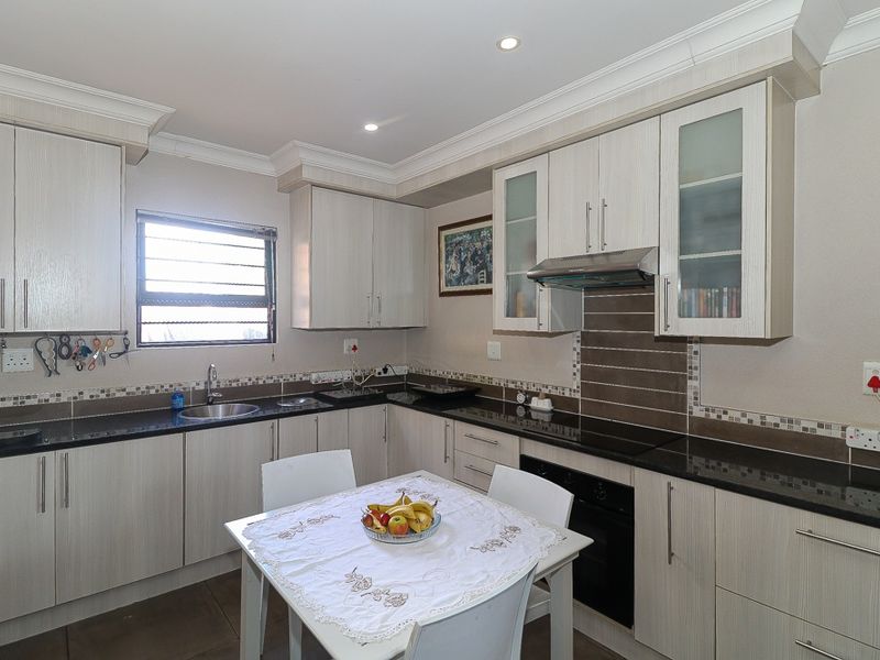 A well-maintained kitchen featuring light wood-grain cabinetry, dark granite countertops, a built-in oven, extractor fan, and a tiled backsplash.